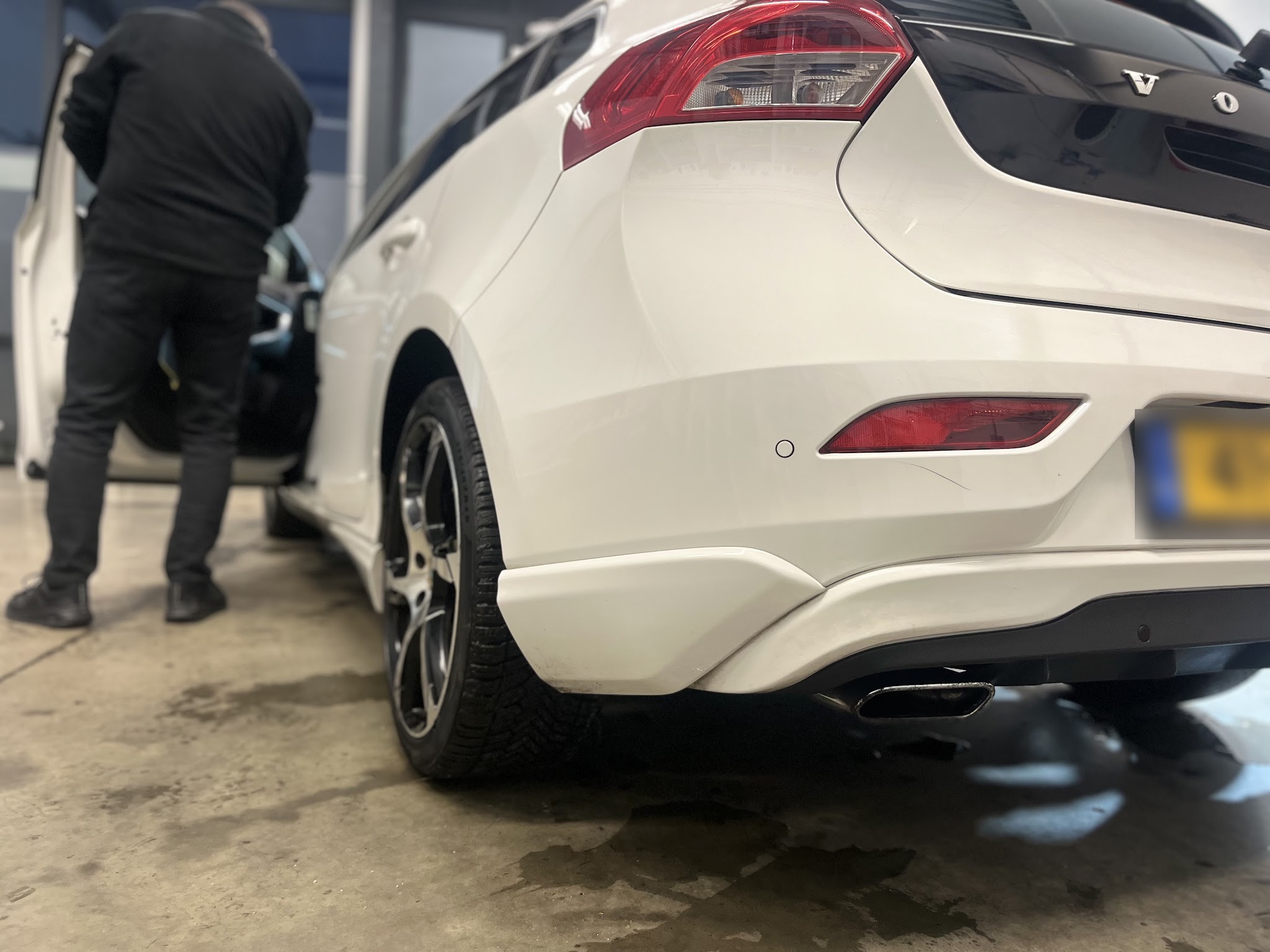 Achterzijde van een witte Volvo V60 in de werkplaats, een klant opent het portier